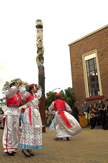 Picture of dancers in traditional Dalmatian costume dancing around the Dalmatian Pou with an orchestra in the background.