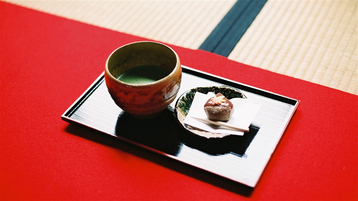 Picture of a ceremonial cup of Japanese tea and plate with a biscuit on a tray. 