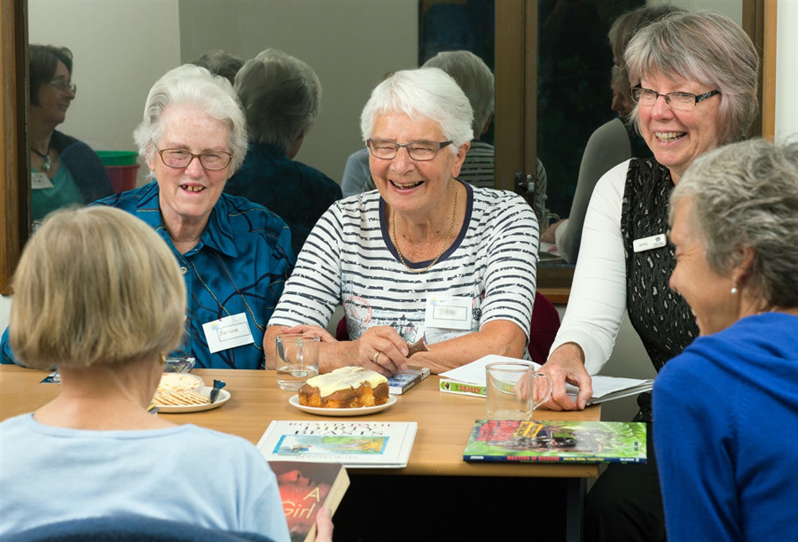 Picture of a group of women sitting around a table discussing books at a book club meeting. 