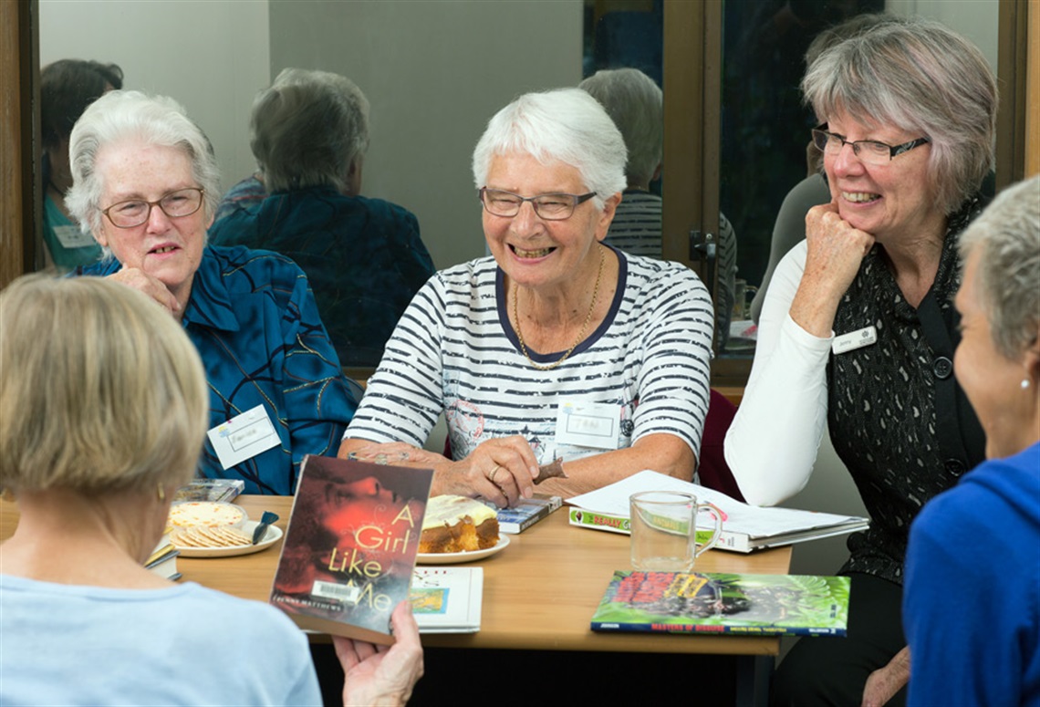 Picture of 5 women sitting around a table discussing books at a book club. 