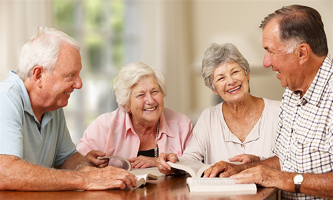 Picture of a book discussion with four elderly people sitting around a table. 