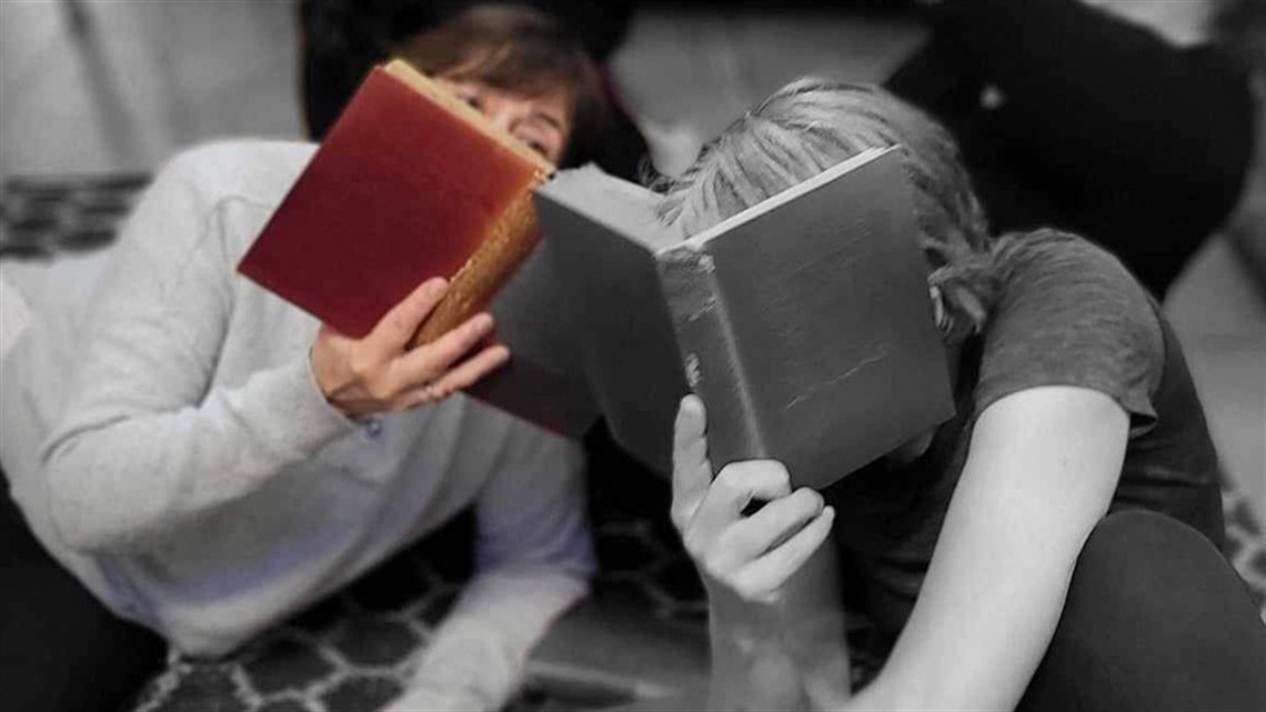 Photo of two people, holding a book each which hides their faces. 