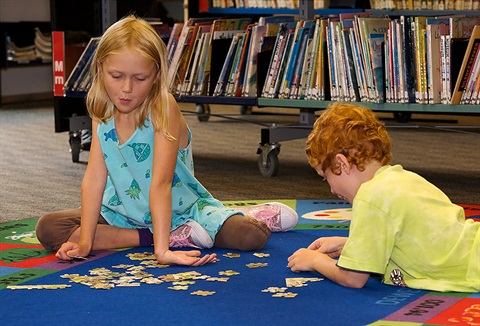 Picture of a girl and boy doing a jigsaw puzzle in a library. 