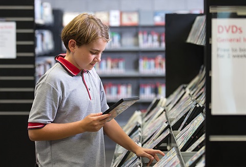 Picture of a girl looking at the Movie DVD collection in a library. 