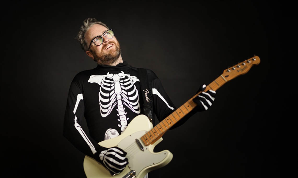 Photo of Gerry Paul with a guitar and dressed in a skeleton costume. 