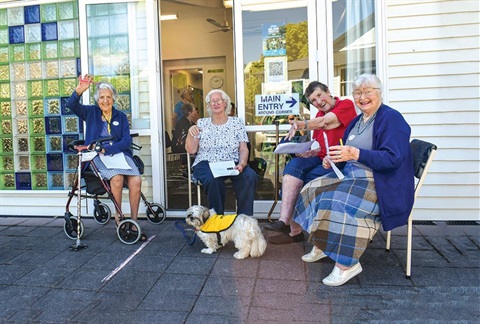 A photo of four older adults sitting together with a grey and white dog. 