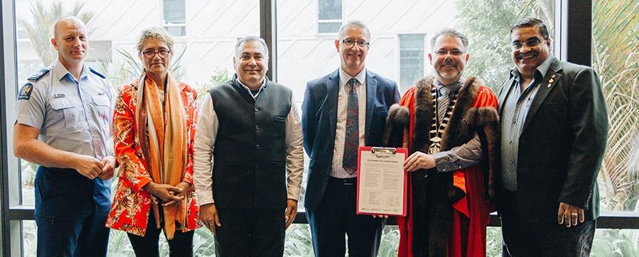 Five people standing behind a table holding the Welcoming Communities Statement of Commitment.