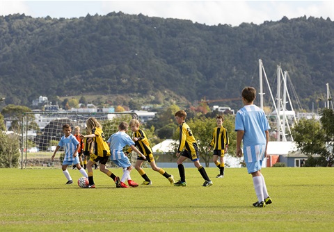 Two boys teams play soccer on a green sportsfield with mountains in the background. 