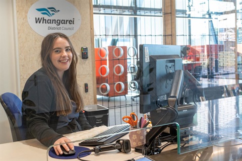 A customer service representative sitting smiling at the counter desk. 