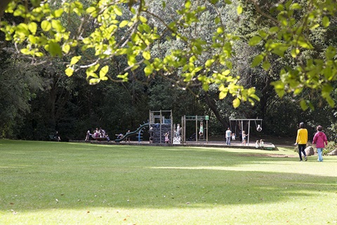 A photo of Mair Park with green grass, trees and children playing on the playground. 