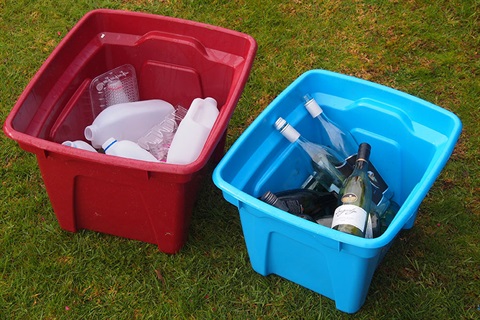 A photo of blue glass recycling bin next to a red plastics recycling bin.