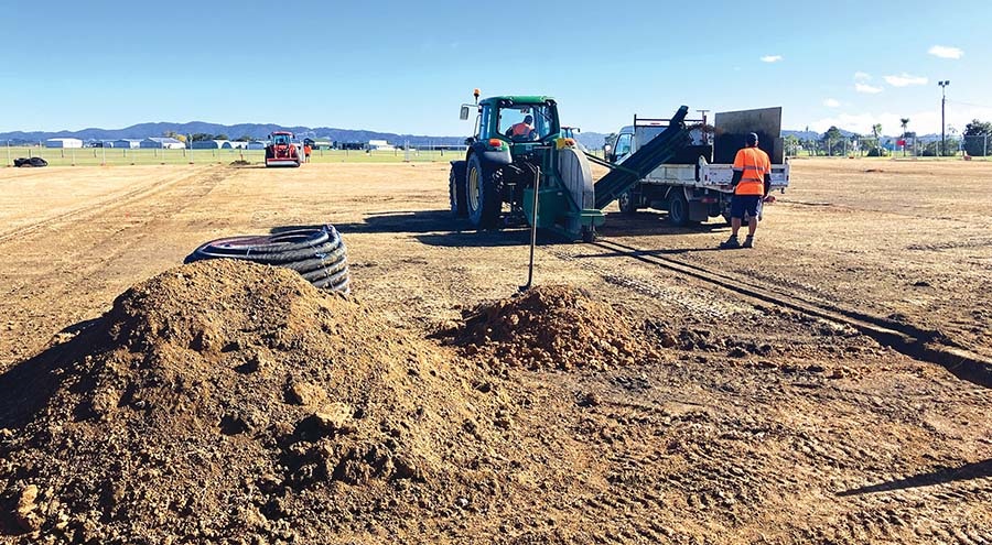 Work progresses on the Onerahi sportsfields with piles of dirt and people working.