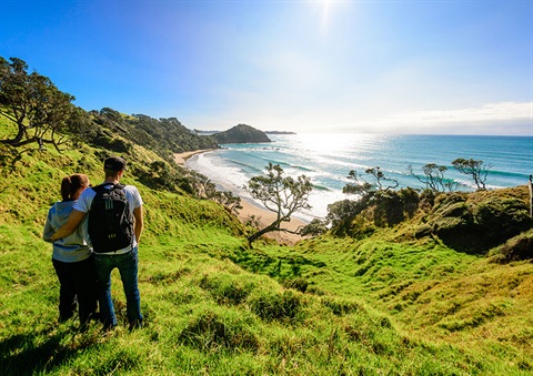 A couple wearing small backpacks look out over Daisy Bay, Tutukaka. 