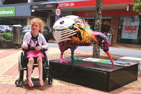 A young girl in a wheelchair sits next to a kiwi sculpture in Whangārei central city on the Kiwi Art Trail. 