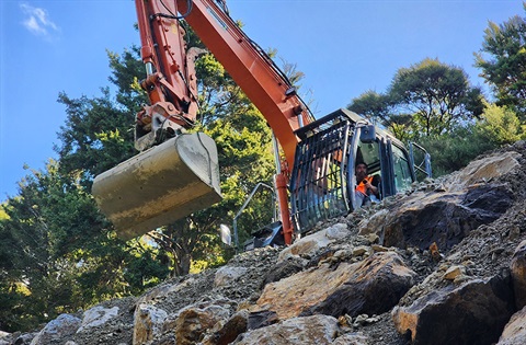 An orange digger in operation over a steep rocky bank. 