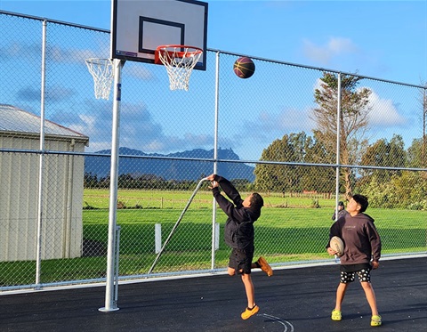 Two boys play on the new basketball court, shooting hoops.