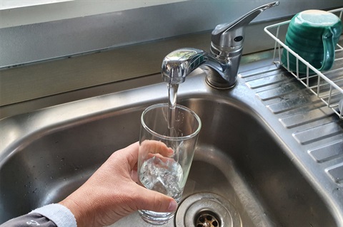 A person pouring a glass of water from the tap at the kitchen sink. 