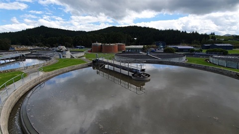 Whangarei's Wastewater Treatment Plant with water at the top of a wastewater tank in the foreground reflecting the sky and other tanks between it and hills in the background. 