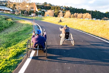 Two riders on adaptive bikes at the Bike Park circuit track on Pohe Island.