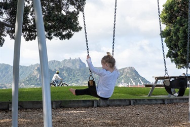 Child on a swing at the playground at the Marsden Bay reserve, One Tree Point and the views across the harbour.