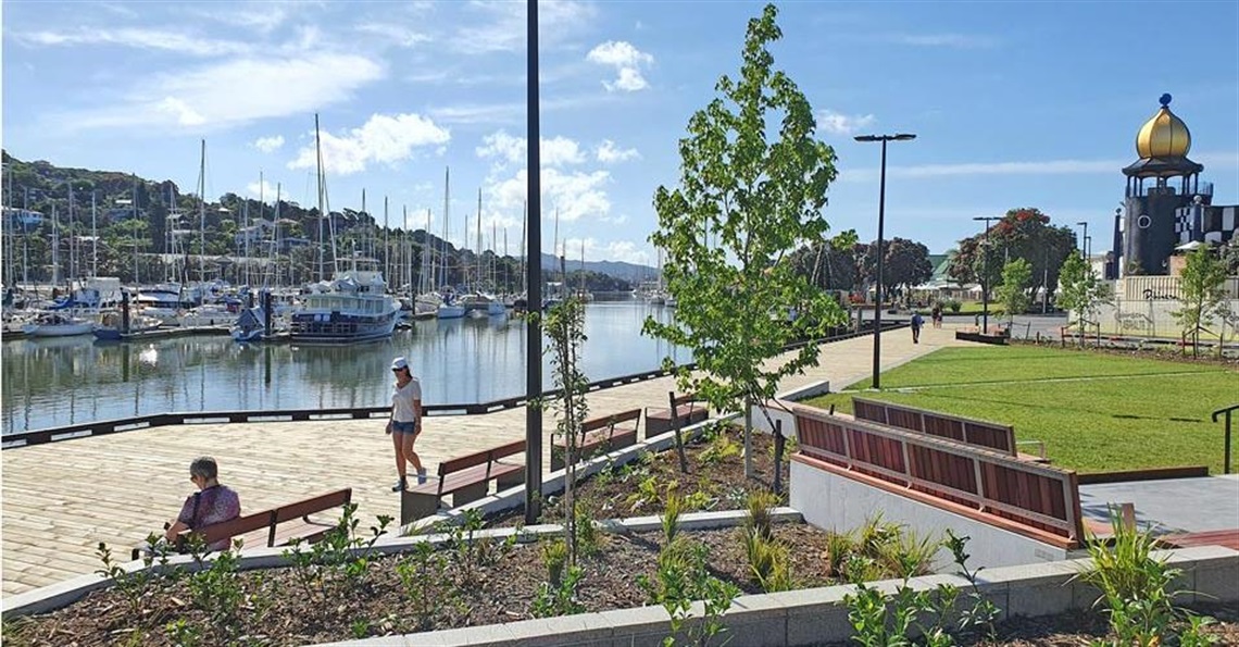 Photograph showing the Town Basin Park, the Hatea River, a boardwalk and the dome of the Hundertwasser Art Centre in the background. 