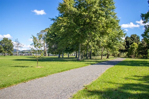 Tikipunga Sports Park photo showing a gravel path, sports-fields and shady areas under leafy trees. 